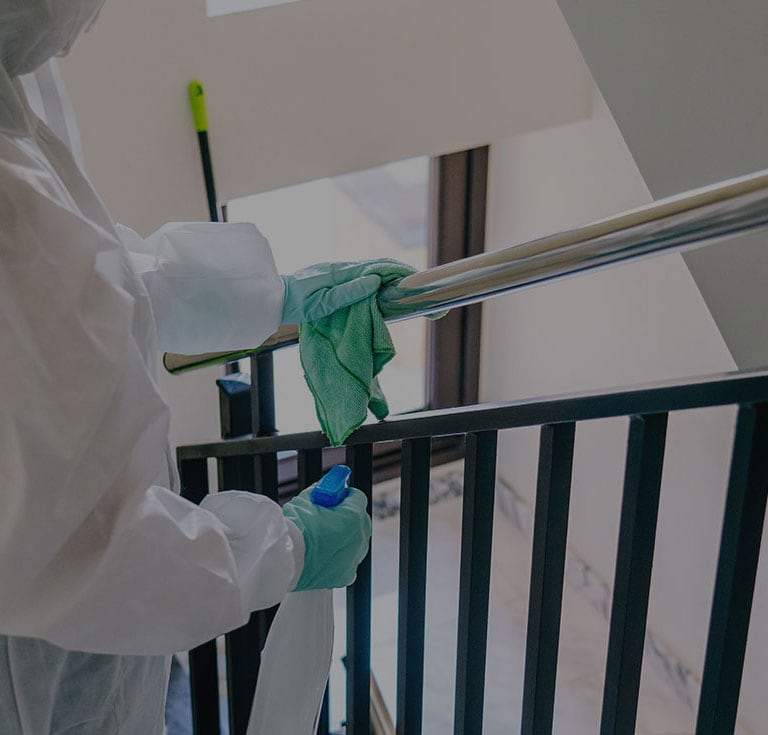 person wearing protective gear sanitizing a stair bannister