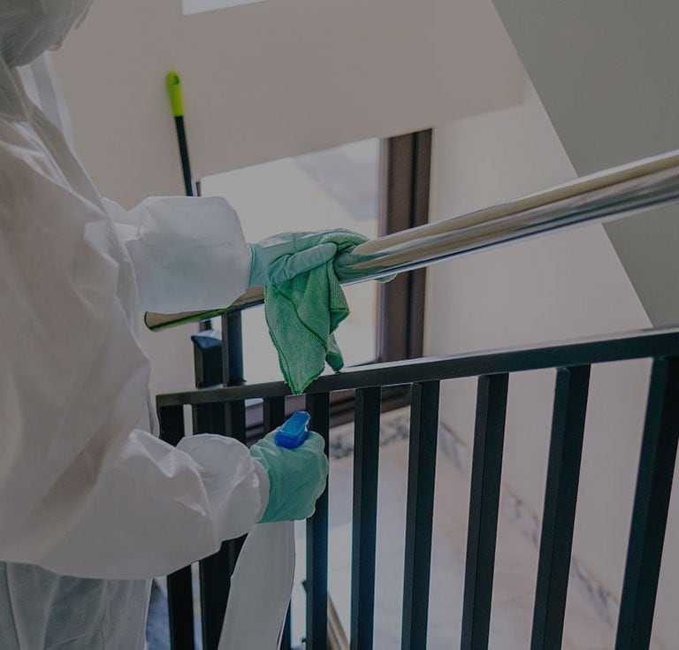 worker in protective clothing wiping a stair bannister